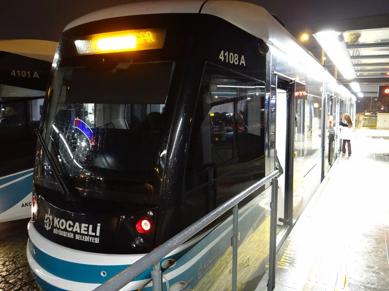 İzmit'te akşam saatinde durakta bekleyen Kocaeli Büyükşehir Belediyesi tramvayı ve peronda bekleyen yolcu